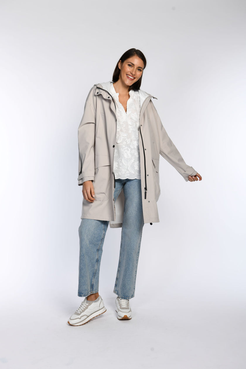 Beiger Regenparka offen getragen, weiße Bluse darunter sichtbar.