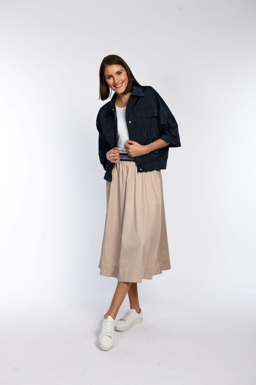 Model trägt einen beigefarbenen Rock in Kombination mit einer locker geschnittenen Jacke in Blau.