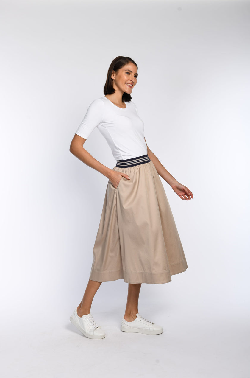 Model trägt einen beigefarbenen Rock aus satinierter Ware mit seitlichen Eingriffstaschen.