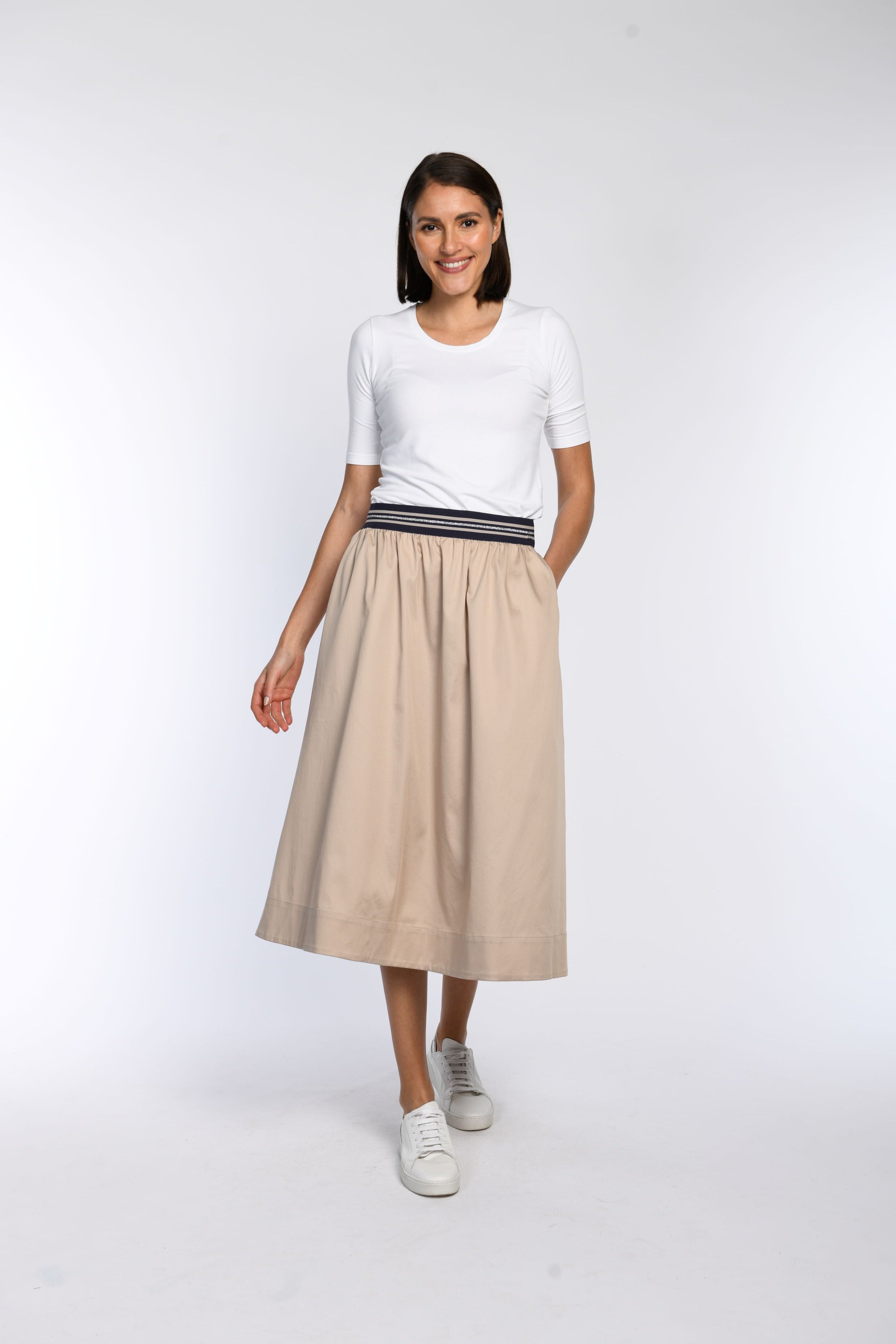 Model trägt beigen Rock in A-Linie mit gestreiftem Gummibund und schrägen Eingriffstaschen.