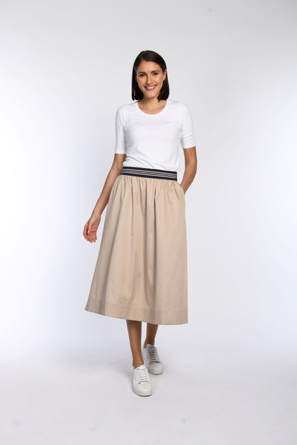 Model trägt beigen Rock in A-Linie mit gestreiftem Gummibund und schrägen Eingriffstaschen.
