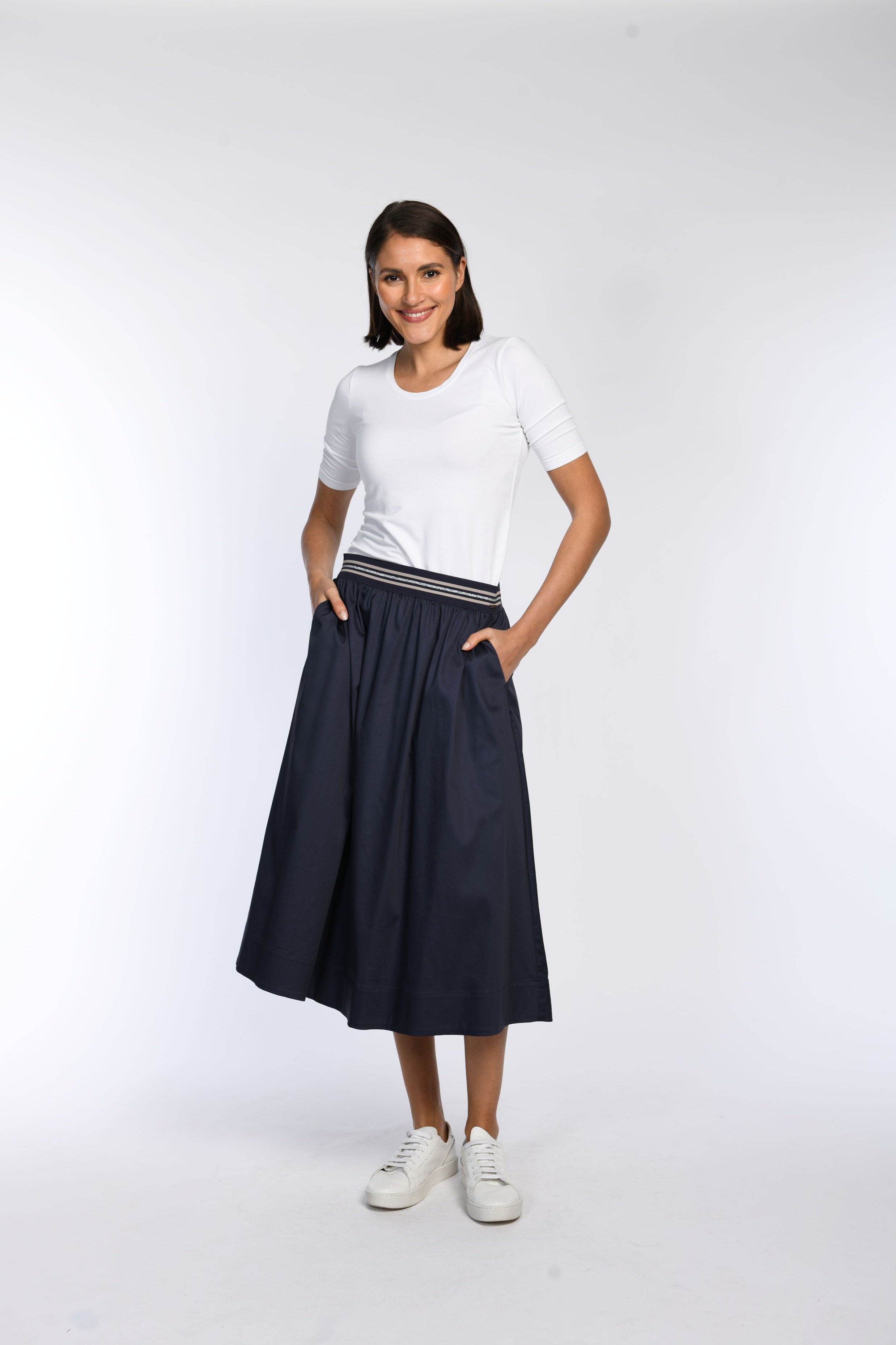 Model trägt blauen Rock in A-Linie mit gestreiftem Gummibund und schrägen Eingriffstaschen.