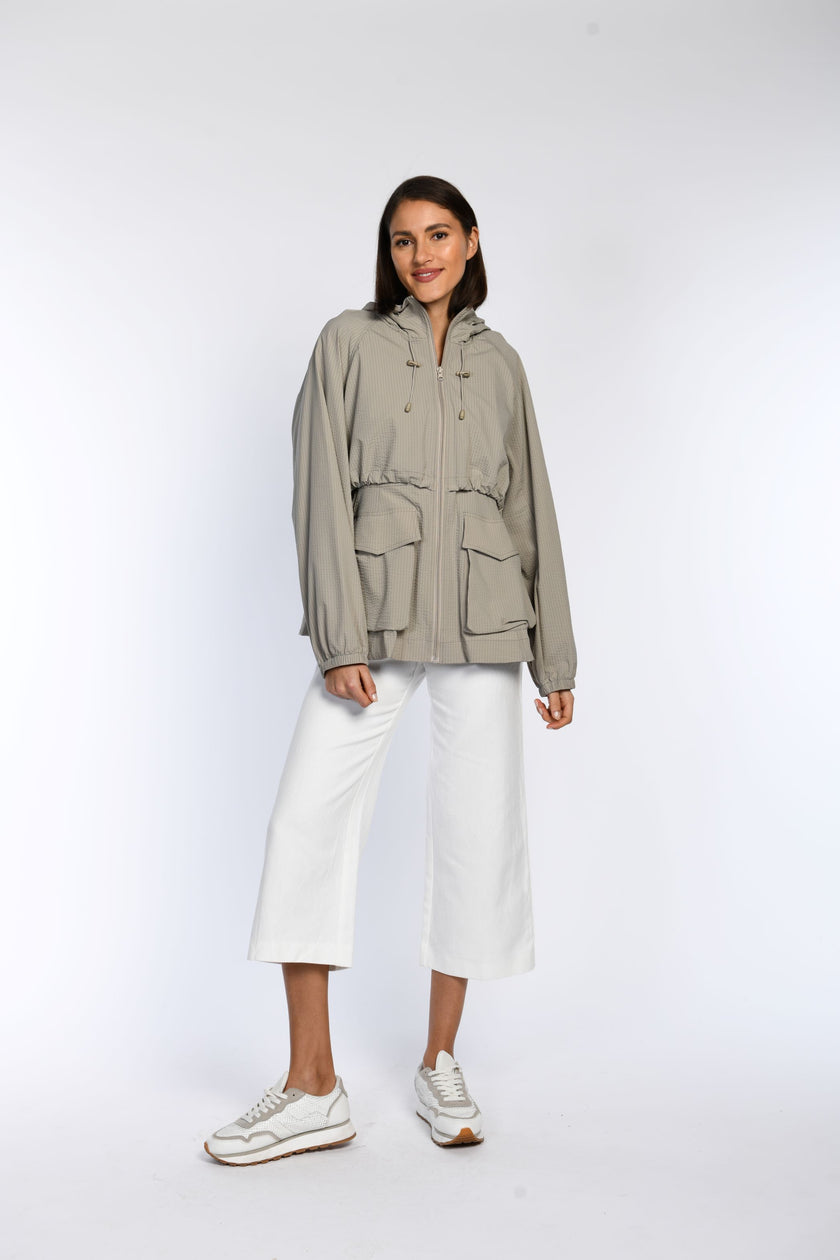 Model trägt eine geschlossene, sommerliche Jacke in Taupe mit zwei Seitentaschen und elastischen Bündchen an den Ärmeln.