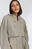 Nahaufnahme eines Models in einer leichten, taupefarbenen Jacke mit Kapuze und sichtbaren Seitentaschen.