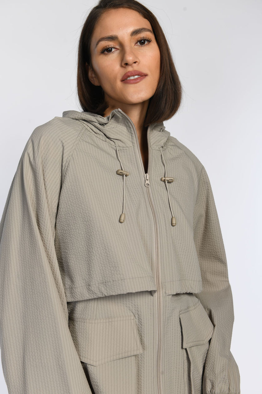 Nahaufnahme eines Models in einer leichten, taupefarbenen Jacke mit Kapuze und sichtbaren Seitentaschen.