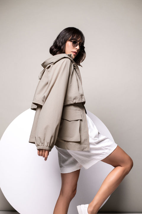 Seitenansicht: Model trägt leichte taupefarbene Kapuzenjacke mit elastischen Ärmelbündchen.