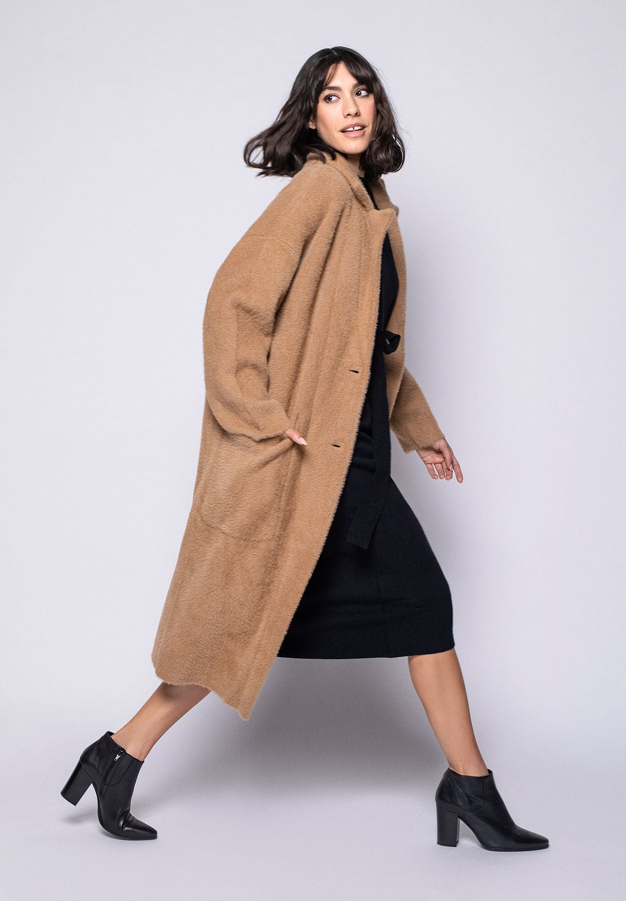 Model trägt knielangen braunen Strickmantel für Damen lässig kombiniert zu schwarzem Kleid – Seitenansicht rechts