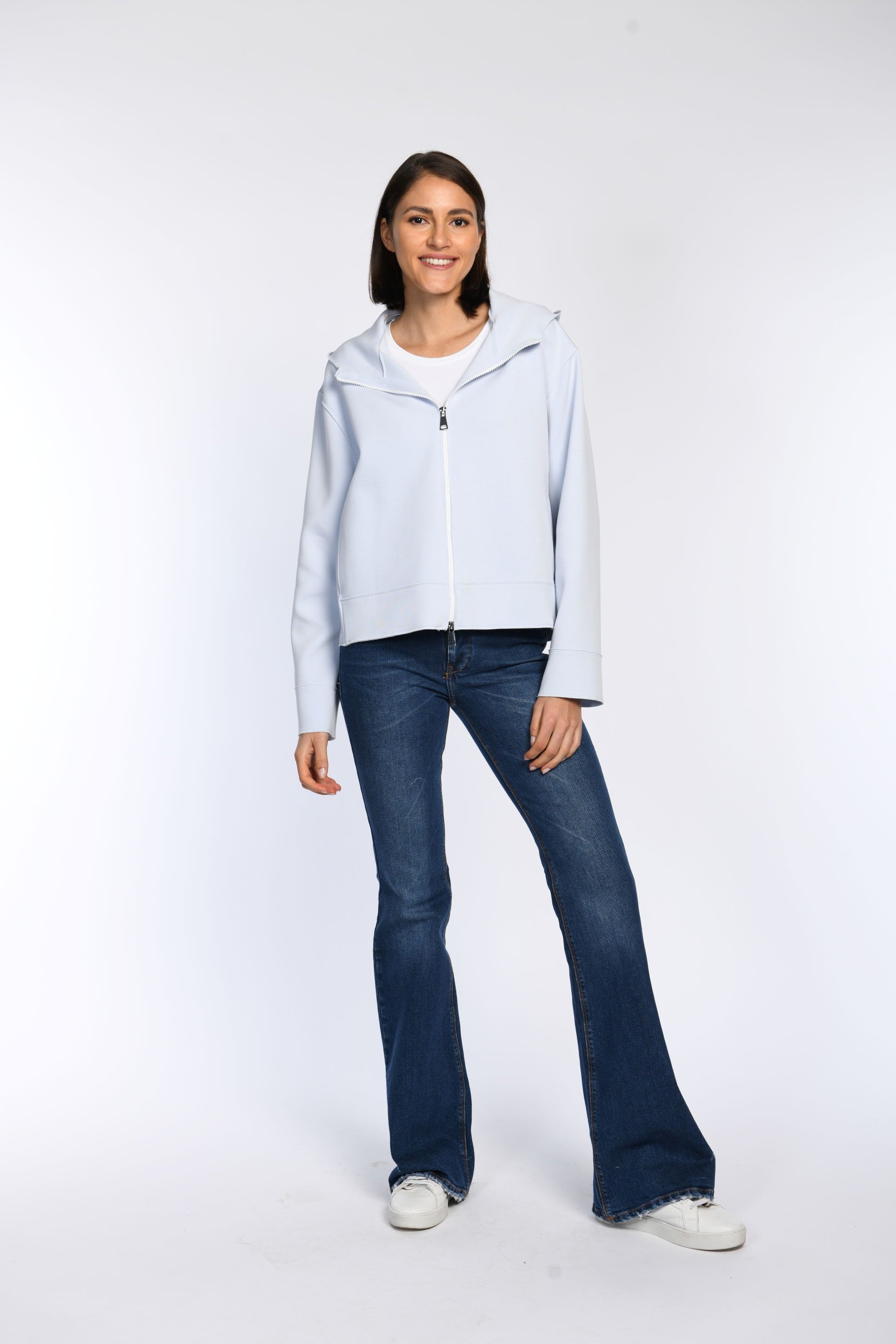 Ein Model trägt eine geschlossene, hellblaue Sweatjacke mit Kapuze und einem sichtbaren Zwei-Wege-Reißverschluss.